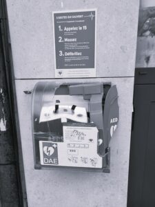 Défibrillateur DAE sous une affiche expliquant les trois gestes qui sauvent : appeler, masser, défibriller
